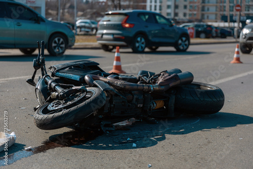 A wrecked motorcycle (bike) lies on its side on the asphalt after a traffic accident. It lies on the roadway after an accident. The headlight and handlebars are broken. Hazard and insurance concept.