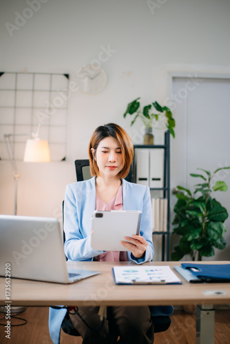 Photos Confident Asian businesswoman multitasking with tablet and laptop in bright office