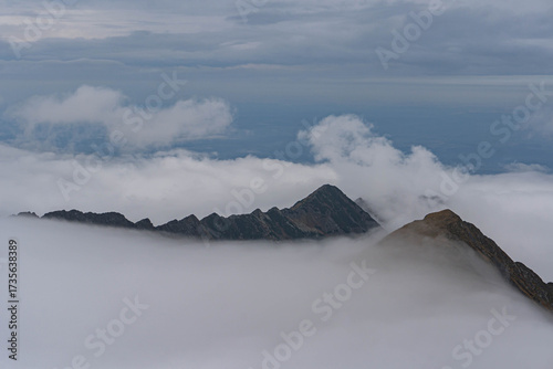 view of highest peaks of romanian carpathian ridge chain from top on very cloudy day with fluffy white clouds at bottom