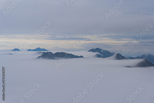 view from moldoveanu of highest peaks of romanian carpathian ridge chain from top on very cloudy day with fluffy white clouds at bottom
