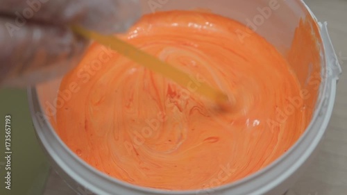 Hand stirs liquid paint in tin. Selective focus.