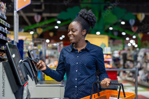 Obraz na plátně Young black woman scanning groceries and paying with a smartphone at a supermark
