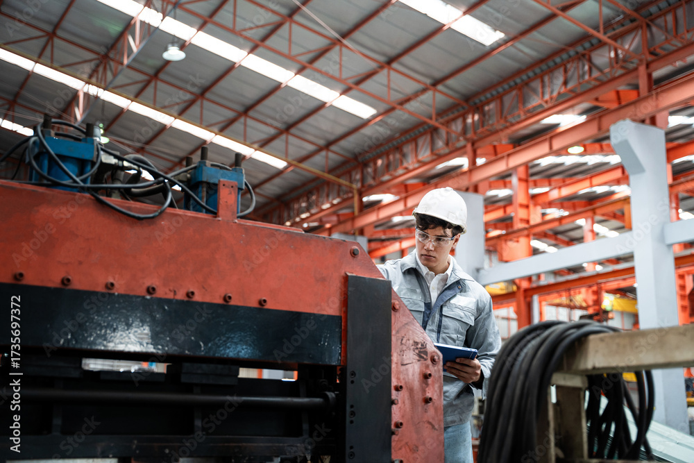 Fototapeta premium A man in a white helmet is looking at a machine in a factory