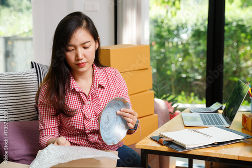 Young woman packing ceramic plate with bubble wrap for safe delivery, working from home in small business e-commerce shipping and online retail.