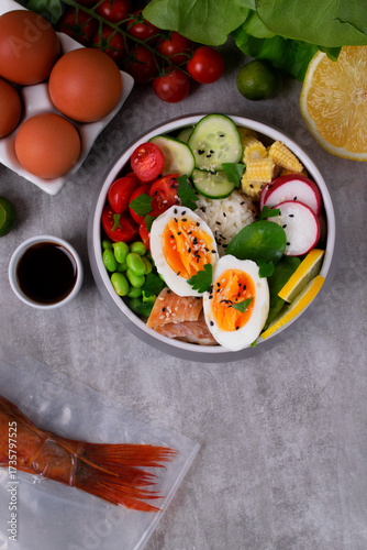 Poke bowl with smoked redfish, eggs, vegetables, edamame beans and rice served on gray table. Healthy balanced meal with white fish. Top view