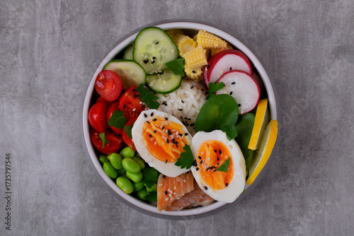 Poke bowl with smoked redfish, eggs, vegetables, edamame beans and rice served on gray table. Healthy balanced meal with white fish. Top view