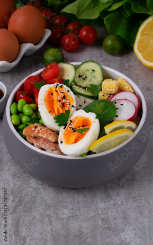 Poke bowl with smoked redfish, eggs, vegetables, edamame beans and rice served on gray table. Healthy balanced meal with white fish
