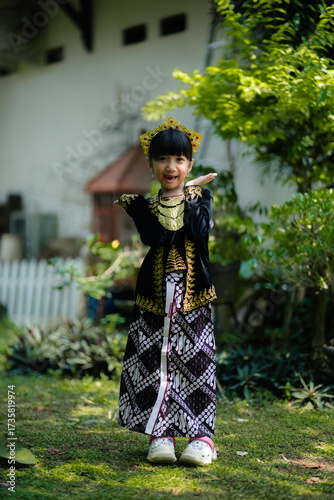 A young girl in traditional Javanese kebaya with batik skirt and golden crown accessory smiling outdoors. Perfect for culture, education, and heritage concepts.