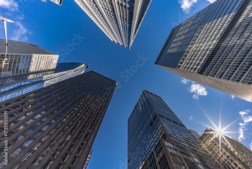 Street level view of highrise buildings with sunburst at 6th Ave & W 53rd St, Manhattan cityscape.