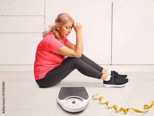 Quadro su tela Mature woman sitting on the ground with a weight scale
