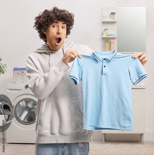 Schilderij op canvas Surprised young man holding a blue t-shirt