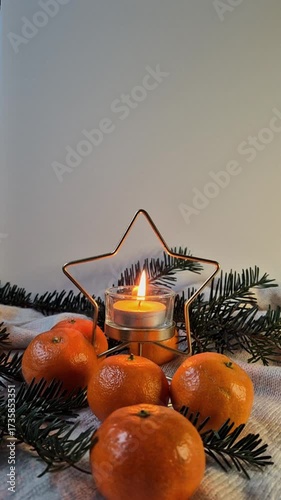 Candle in a glass candlestick with a stylized golden star surrounded by tangerines on a white background with fir branches. Cozy festive atmosphere perfect for winter holidays and Christmas decor slow