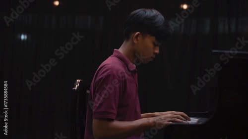Young Man Playing Grand Piano on Stage Under Dramatic Lighting Music Concert or Recital Scene