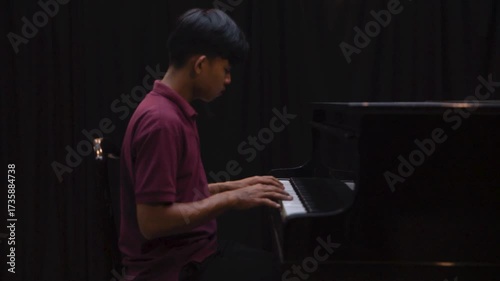 Young Man Playing Grand Piano on Stage Under Dramatic Lighting Music Concert or Recital Scene