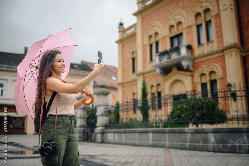 Fototapeta premium Tourist taking photos in the rain with pink umbrella