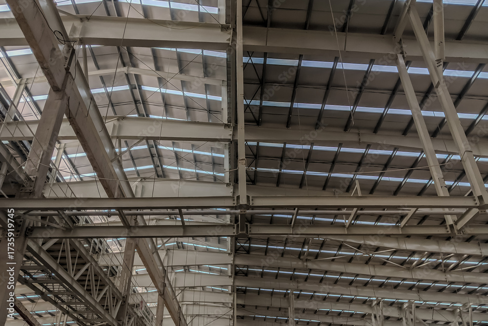 Obraz premium Interior view of industrial warehouse roof with steel beams, trusses, and skylight panels providing natural lighting.