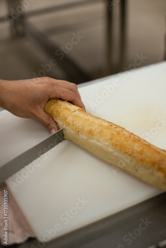 Person slicing fresh baguette on a cutting board in a bakery kitchen