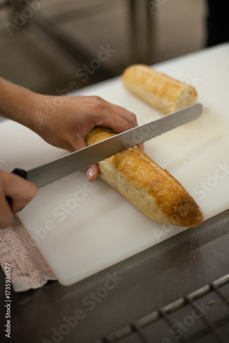 Person slicing fresh baguette on a cutting board in a bakery kitchen