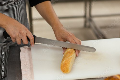Person slicing fresh baguette on a cutting board in a bakery kitchen