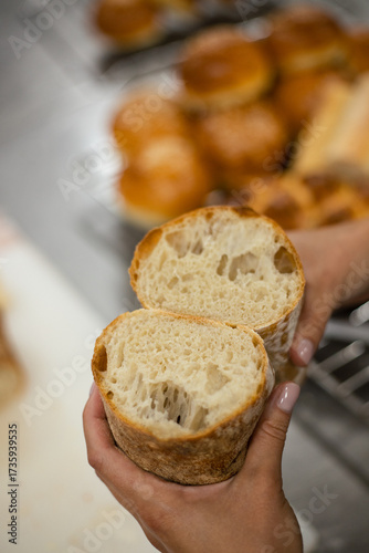 Woman holding freshly baked artisan bread cut in half, showing soft airy crumb and crispy crust. Homemade sourdough loaf in bakery kitchen.