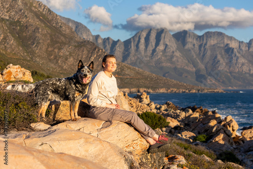 A woman with an Australian Cattle Dog (Blue Heeler) outdoors exploring together with ocean and mountain views