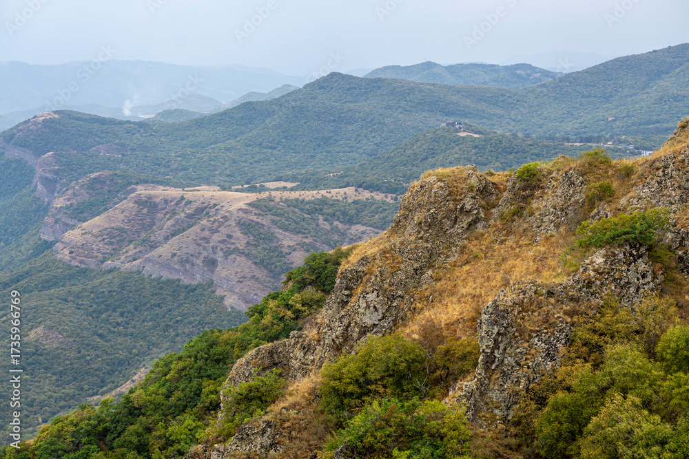 Fototapeta premium Mountain and hilly landscape. Green trees and bushes. Field with faded grass. Rock in the foreground. Azeula fortress. Kojori
