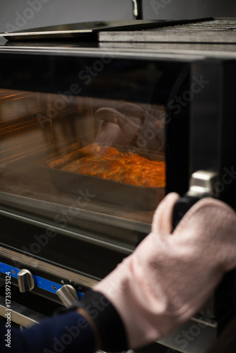 Person wearing oven mitts takes freshly baked focaccia with salt out of the oven.