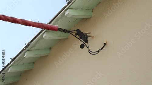 Détail d'un câblage électrique fixé sous un toit en bois dans un environnement résidentiel en plein jour.