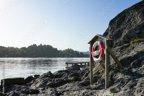 Lifebuoy station on rocky shore by the water. Norway.