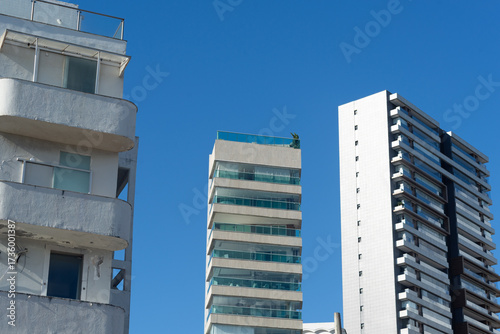 View of tall, modern buildings with balconies and glass facades under a clear blue sky
