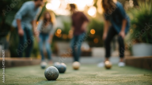 Group of four people playing a game of bocce ball on a green artificial turf. the background is blurred, but it appears to be an outdoor setting with trees and plants.
