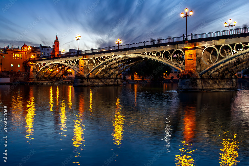 Obraz premium Dusk at Triana Bridge with glowing reflections in Seville