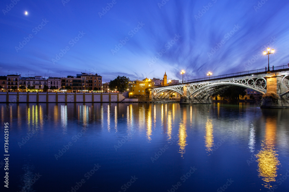 Naklejka premium Crescent moon rises over Triana Bridge at dusk in Seville
