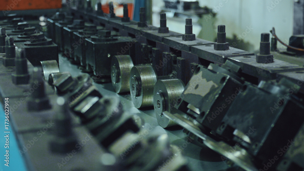 Obraz premium Industrial machinery forming a metallic sheet into a specific profile using a series of precisely aligned shaping rollers, representing modern factory automation and engineering processes