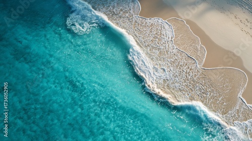 Overhead perspective captures a tranquil beach scene, featuring waves gently rolling onto the sandy shore, creating a serene atmosphere; the clear turquoise ocean meets the beige sand, showcasing...