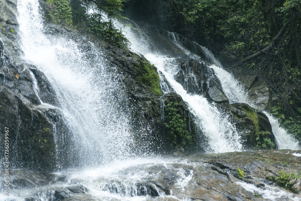 Fototapeta premium Impressive waterfall demonstrates raw power of nature, where water flows and cascades over dark rock. forest vibrant green creates natural stream, offering truly refreshing and peaceful outdoor