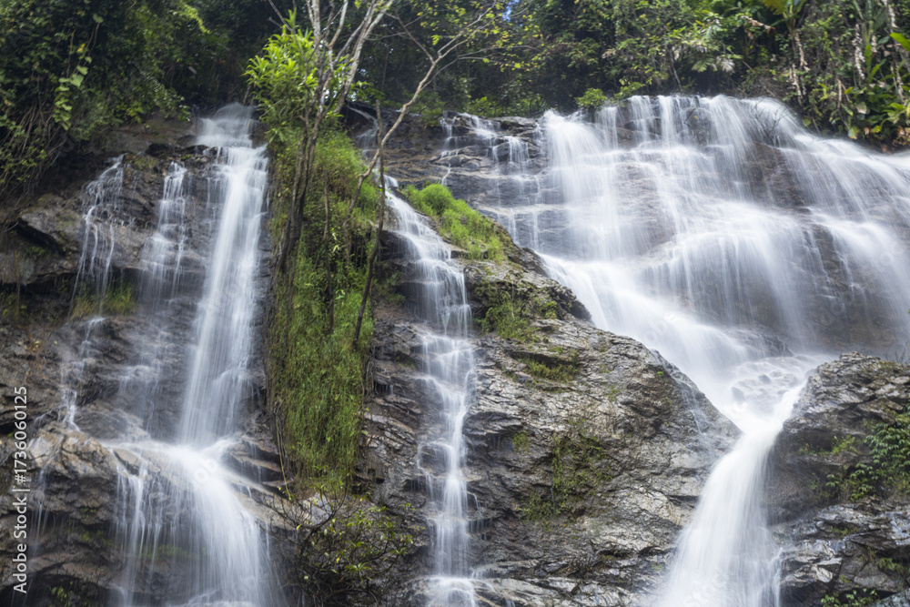 Fototapeta premium Tropical waterfall cascades over rugged rock formations within lush green forest landscape. natural environment evokes serene feelings, powerful scene of untouched wilderness and peace