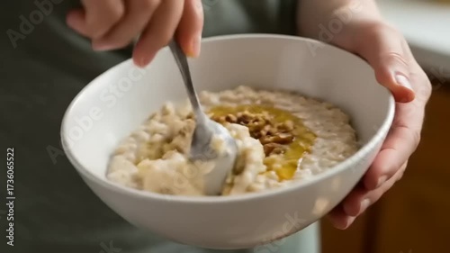 Close-up of a person stirring oatmeal in a bowl with honey and walnuts, cozy kitchen setting