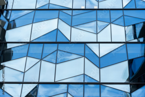 Contemporary building facade with geometric blue glass panels with angular shapes and reflective surfaces. For illustrating modern architecture, urban design, and innovative construction concepts.