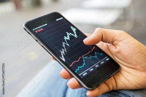 Hand Holding Smartphone and Tapping Screen to Analyze Live Financial Stock Market or Cryptocurrency Trading Chart and Investment Data