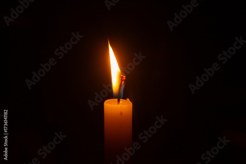 Close up na chama acesa de uma vela com fundo escuro.