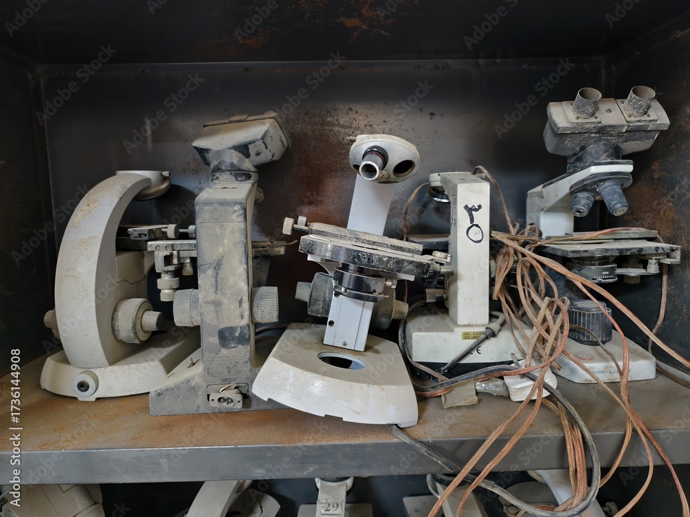 Fototapeta premium Basrah, Iraq - October 1, 2025: Close-up of old, dusty microscopes with tangled wires on shelves.
