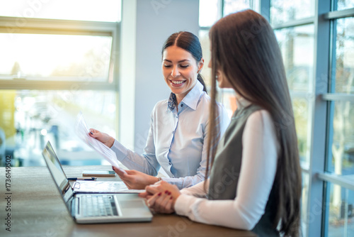 Free Download Female colleagues discussing business strategy while reviewing documents in bright modern office - GFXLoad