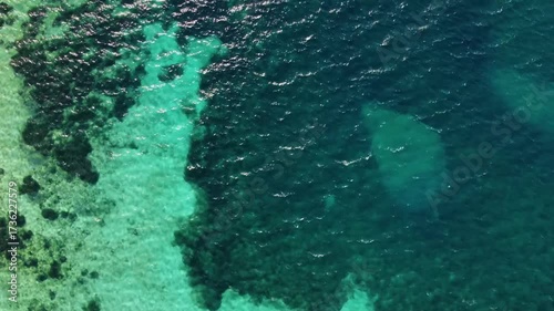 aerial perspective captures the crystal clear turquoise waters of the Mediterranean Sea, transitioning into deeper blue hues along the coast near the ancient city of Knidos, Turkey. The footage showca
