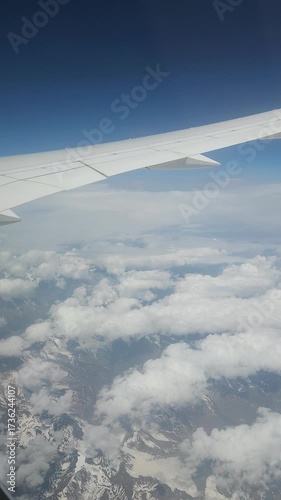view of wing from plane window. Airplane flying above clouds. Airplane fly over snowy mountain hills. vertical video