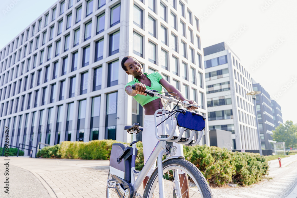 Obraz premium Happy Black woman leaning on bicycle handlebars in city environment