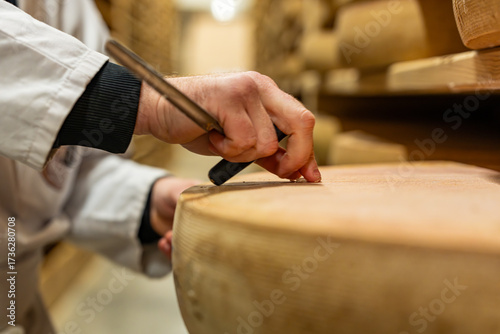 Main coupant un morceau de fromage affiné dans une cave à fromage traditionnelle, illustrant un geste artisanal et la dégustation d’un produit laitier dans un environnement de maturation.