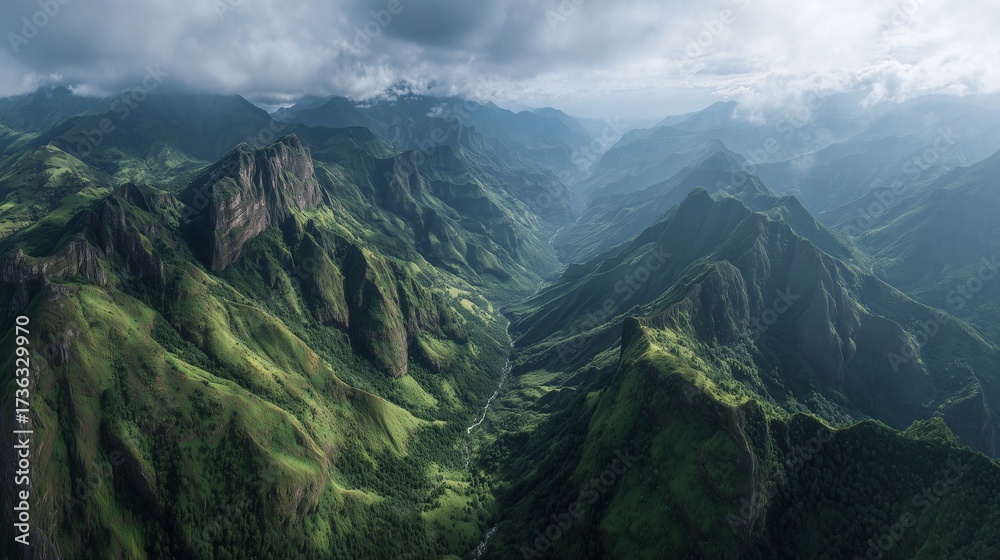 Naklejka premium Green mountains rise sharply, with the green slopes cascading into valleys below. Shadows from clouds cover the green terrain, blending into the mountainous landscape.