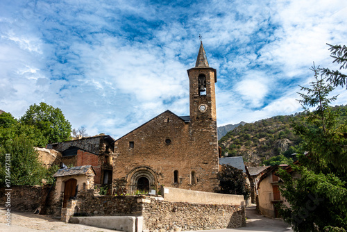 A picturesque view of the ancient Romanesque church of Sant Lliser d'Alós d'Isil, nestled in its traditional mountain village in the Spanish Pyrenees. Catalonia