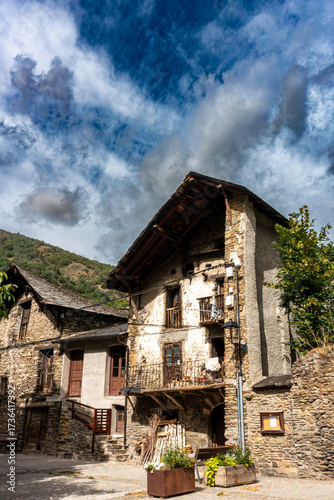 A traditional rustic stone house in the Pyrenean mountain village of Alós d'Isil under a dramatic, cloudy sky. Catalonia, Spain.